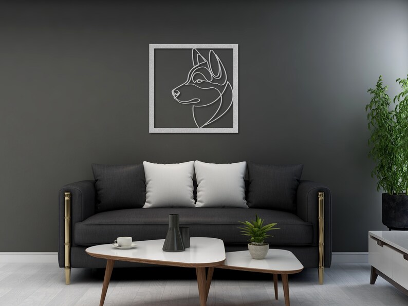 Pode incluir: Um sof&aacute; preto com duas almofadas brancas e uma moldura de metal dourado fica em frente a uma parede cinza escura. Uma impress&atilde;o de arte de linha emoldurada de uma cabe&ccedil;a de cachorro est&aacute; pendurada na parede. Uma pequena mesa de caf&eacute; branca com uma base de madeira fica em frente ao sof&aacute;. Uma pequena planta em vaso fica sobre a mesa.