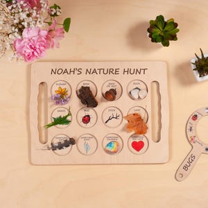 May include: A rectangular wooden nature hunt board with the text NOAH'S NATURE HUNT. It features twelve circular cutouts labeled with items like flower, bark, seed or nut, rock, grass, bug, stick, leaf, something soft, shiny, colorful, and something you love.