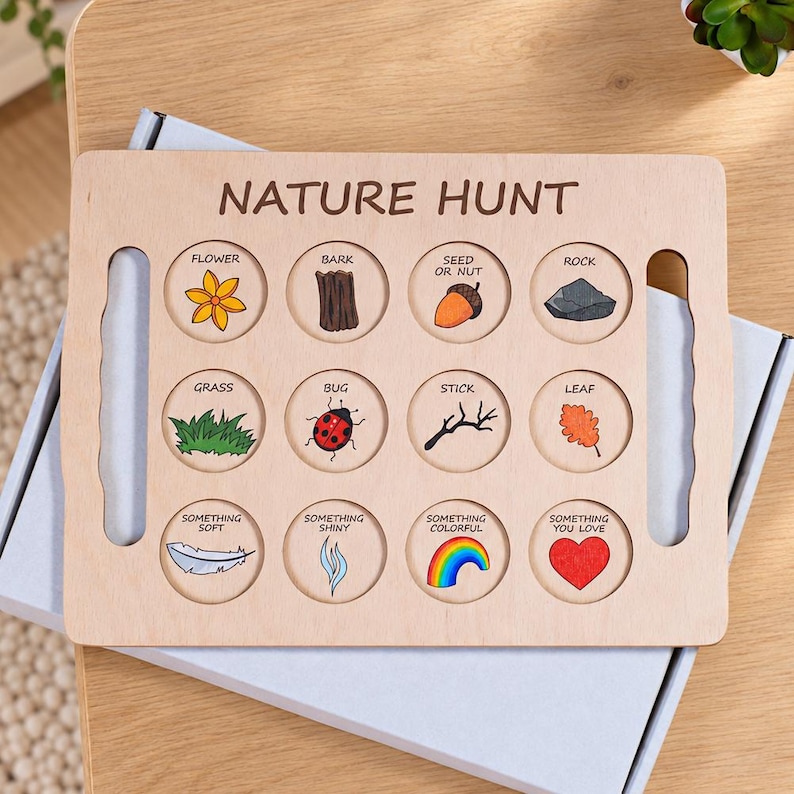May include: A rectangular light-colored wooden nature hunt board featuring the text NATURE HUNT at the top. It contains twelve circular cutouts with illustrations and labels for items like a flower, bark, seed, rock, grass, bug, stick, leaf, and more.