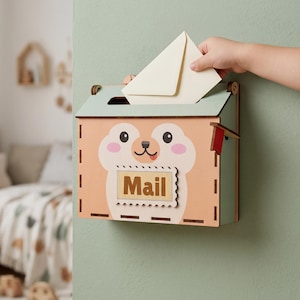 Peut inclure: Une boîte aux lettres murale en bois avec une finition pêche clair et vert menthe, ornée d'un visage d'animal. L'avant présente une étiquette rectangulaire avec le mot Mail en lettres marron et un petit drapeau rouge sur le côté.