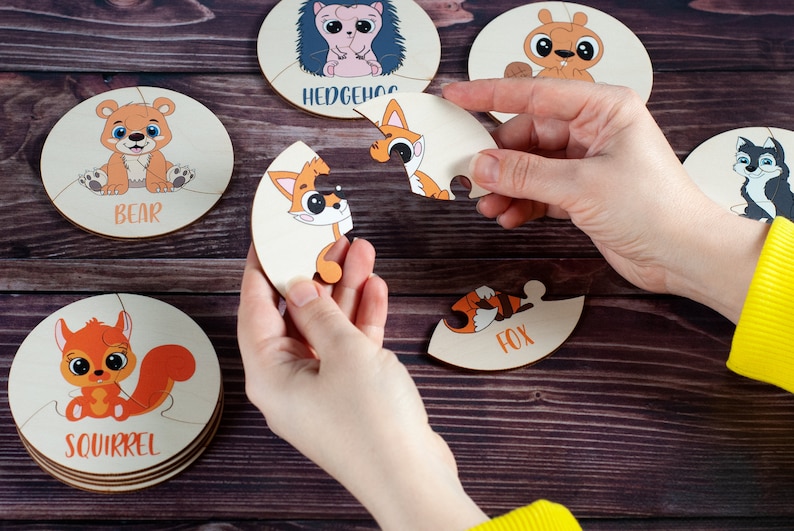 Może przedstawiać: Zestaw sześciu drewnianych puzzli przedstawiających r&oacute;żne zwierzęta, w tym niedźwiedzia, jeża, lisa, wiewi&oacute;rkę i dwa lisy. Każdy element układanki ma kształt innego zwierzęcia i ma nadrukowaną odpowiednią nazwę.