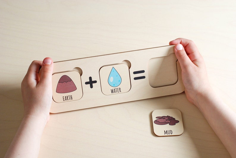 A wooden puzzle with three slots. The first slot has a picture of a brown mountain with the word "Earth" below it. The second slot has a plus sign. The third slot has a picture of a blue water drop with the word "Water" below it. The fourth slot has an equals sign. The fifth slot is empty. A separate wooden piece with a picture of brown mud and the word "Mud" below it is shown on the table.