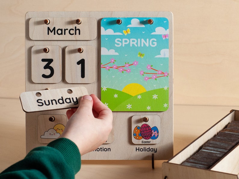 May include: A wooden calendar with removable pieces for the day, date, month, and day of the week. The calendar shows March 31st, Sunday, and a card with the word "SPRING" and a picture of a spring scene. There is also a card with the word "Holiday" and a picture of Easter eggs.
