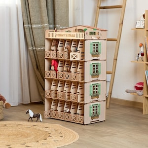 May include: A four-story wooden toy horse stable labeled Tommy's Stable, featuring individual stalls with swinging gates, light wood construction, and printed green window shutters with flower boxes on the side panels, housing several small toy horses.