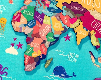 Può includere: Una colorata mappa da parete in legno che raffigura l'Africa e parti dell'Asia con i nomi dei paesi in bianco. L'oceano è di un blu turchese brillante con illustrazioni di una medusa gialla sorridente, stelle marine viola e una balena blu scuro.