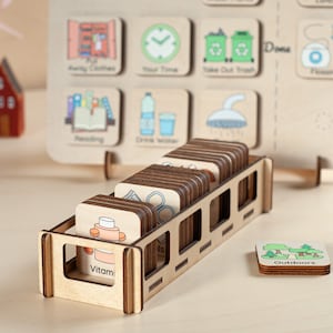 May include: Wooden storage rack with a variety of colourful illustrated cards. The cards feature images of daily activities, such as taking out the trash, drinking water, and reading. The rack is made of natural wood and has a rustic look.
