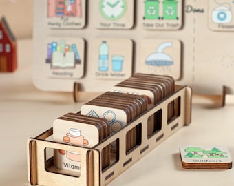 May include: A wooden chore chart with illustrated task cards, including "Away Clothes," "Your Time," and "Take Out Trash." A wooden holder contains additional cards with images like "Vitamins" and "Outdoors."