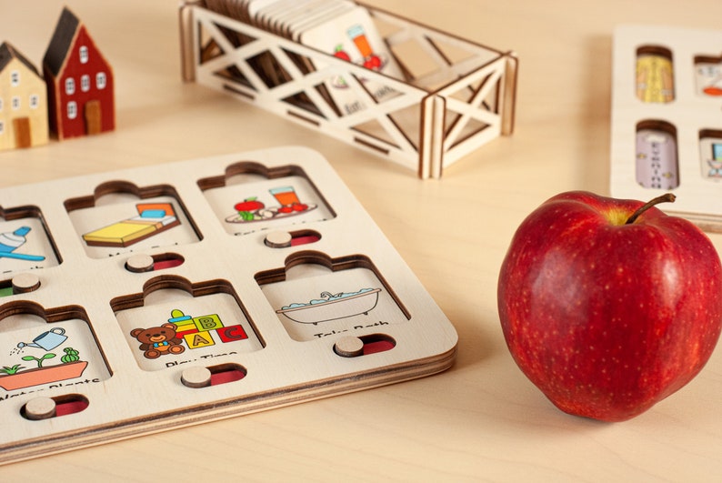 K&ouml;nnte beinhalten: Holzp Puzzle mit bunten Illustrationen von allt&auml;glichen Aktivit&auml;ten wie Schlafen, Essen, Spielen und Baden. Die Puzzleteile sind wolkig geformt und haben ein rot-wei&szlig;-blaues Farbschema. Ein roter Apfel liegt auf einer Holzoberfl&auml;che neben dem Puzzle.