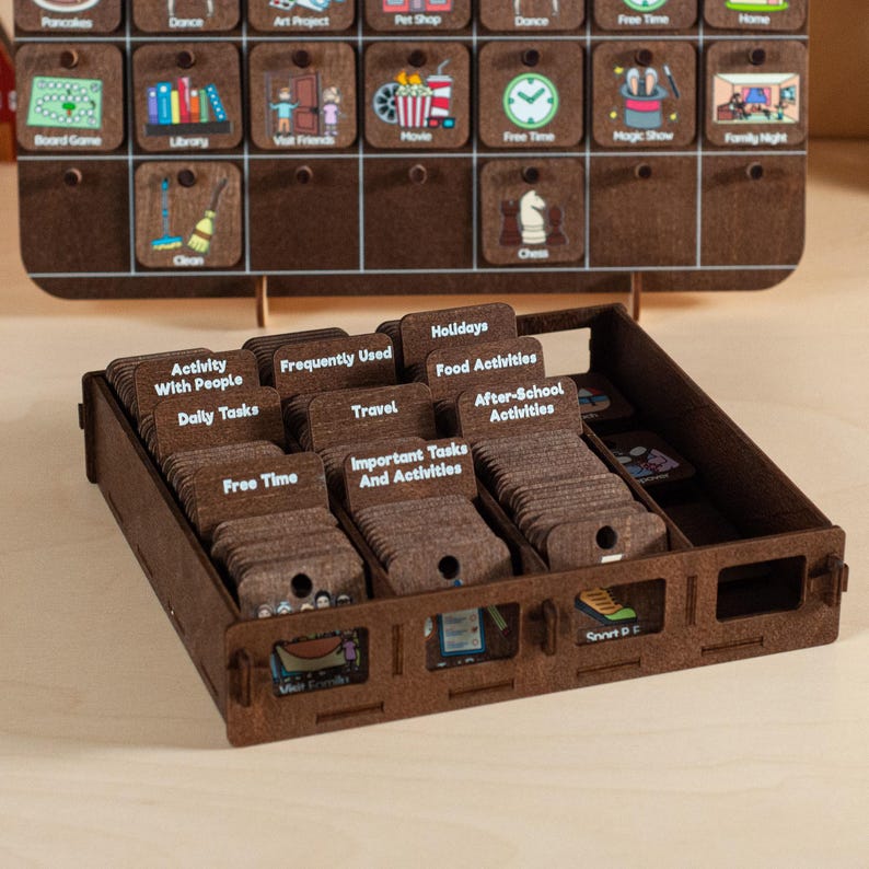 May include: A wooden box filled with small brown cards, each with white text. The cards are organized into categories such as "Activity with People", "Daily Tasks", "Frequently Used", "Travel", "Holidays", "Food Activities", "Important Tasks and Activities", and "After-School Activities".