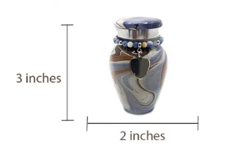 May include: A small, decorative urn with a swirling pattern in shades of blue, brown, and gray. It has a dark blue lid and a beaded accent around the neck. A black heart-shaped charm hangs from the neck. The urn is 3 inches tall and 2 inches wide.