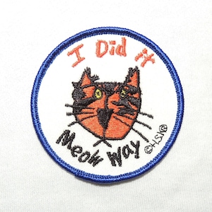 May include: Embroidered patch with a cartoon cat face in orange, black, and white. The patch has a blue border and the text "I Did it Meow Way" in red and black. The patch is round.