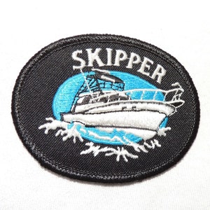 Könnte beinhalten: Schwarzer gestickter Aufnäher mit weißen Nähten, der ein Boot mit dem Wort "SKIPPER" in weißen Buchstaben zeigt.