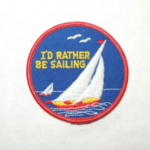 May include: A red, white, and blue embroidered patch with a sailboat and the text "I'd rather be sailing".
