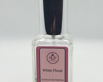May include: A clear glass bottle with a silver cap and a pink label. The label says "White Floral" and "Extrait de Parfum". The bottle contains 1 fl oz (30 ml) of perfume.
