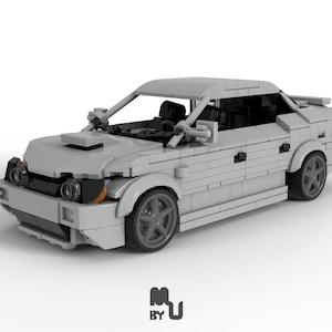 May include: A grey Lego model car with black wheels and a detailed interior. The car has a black windscreen and black headlights. The car is sitting on a white surface.