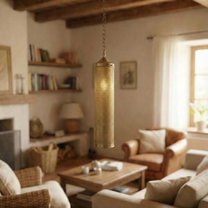 May include: A gold-toned, cylindrical pendant light with a perforated pattern hangs from a chain in a living room. The light is on, and the room includes a fireplace, bookshelves, and comfortable seating.
