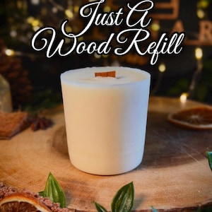 May include: A cylindrical white candle refill with a flat top and a single rectangular wooden wick centered in the wax. The text "Just A Wood Refill" is displayed in a white cursive font with a black outline above the candle.