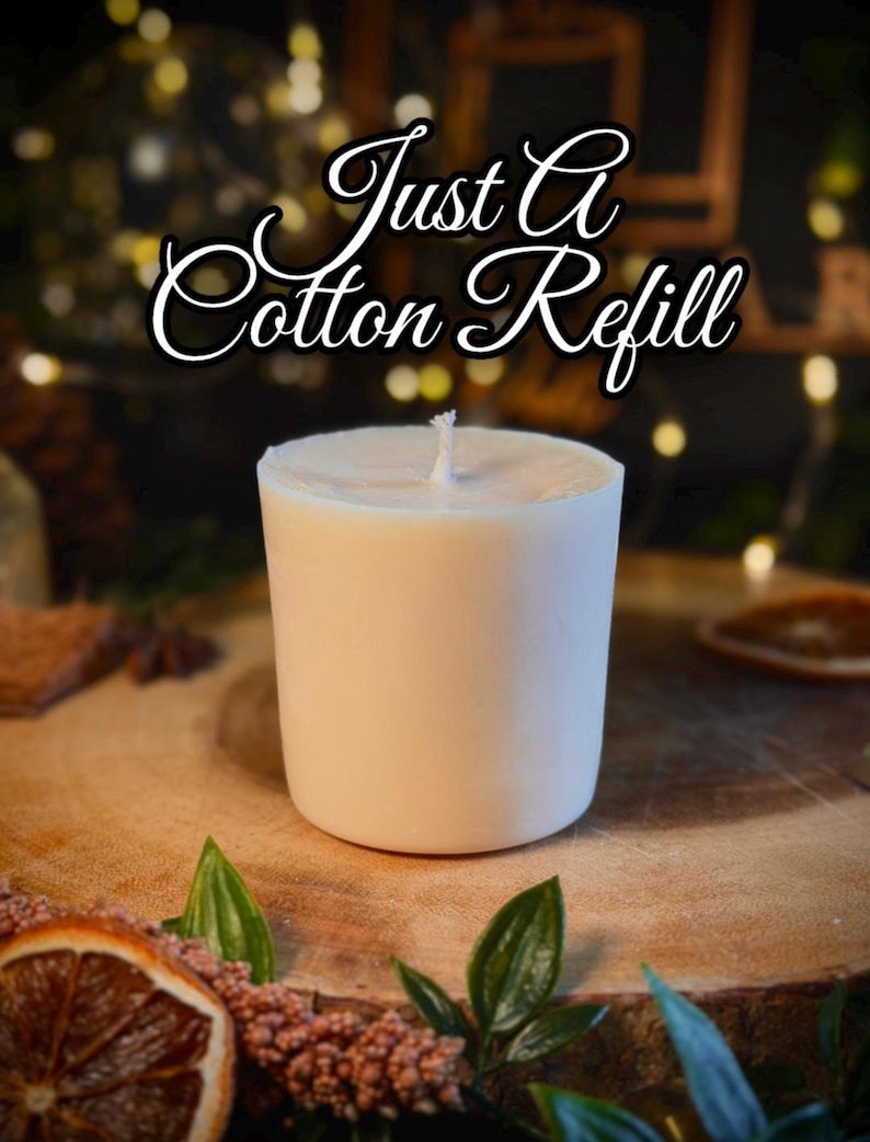 May include: A cylindrical white candle refill with a centered cotton wick. The text "Just A Cotton Refill" is displayed in a white cursive font with a black outline above the candle. The candle has a smooth, solid, opaque wax surface.