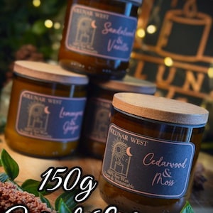 May include: A stack of four glass jar candles with wooden lids. Each candle has a label with the brand name and scent, including "Sandalwood & Vanilla" and "Cedarwood & Moss." The text "150g With Lid" is also visible.
