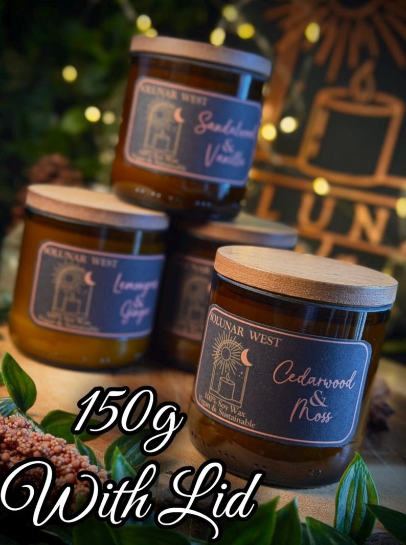 May include: A stack of four glass jar candles with wooden lids. Each candle has a label with the brand name and scent, including "Sandalwood & Vanilla" and "Cedarwood & Moss." The text "150g With Lid" is also visible.