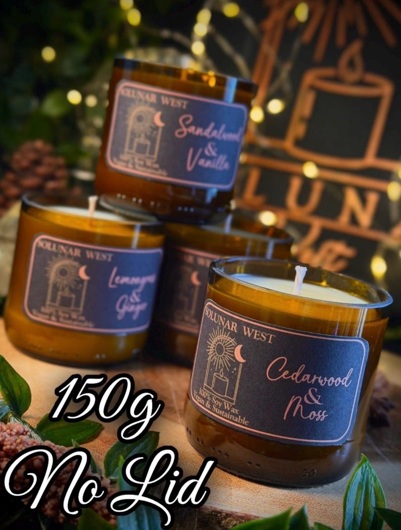 May include: Four glass jar candles with labels reading "Sandalwood & Vanilla", "Lemongrass & Ginger", and "Cedarwood & Moss". The candles are amber-colored with white wicks. The text "150g No Lid" is also visible.