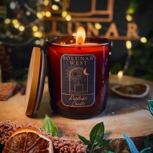 May include: A lit candle in a dark amber glass jar with a wooden lid. The label features the text "SOLUNAR WEST" and "Refillable Candle" with a graphic of a sun, moon, and candle. The flame is visible, and the jar has a deep, warm tone.