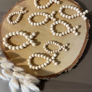 Könnte beinhalten: Eine Holzscheibe mit acht Strängen aus natürlichen Holzperlen, die in einem Kreis angeordnet sind. Die Perlen sind hellbeige und in verschiedenen Größen und Formen angeordnet.