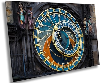 May include: The Prague Astronomical Clock face features a large blue and gold circular dial with Roman numerals, zodiac symbols, and a central sun icon. Intricate stone statues of figures flank the clock, set against a dark, weathered stone wall.