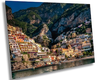 May include: A rectangular wall art print featuring a high-angle landscape view of Positano, Italy. The image displays colorful Mediterranean buildings stacked on a steep cliffside, overlooking the dark blue water of the Tyrrhenian Sea.