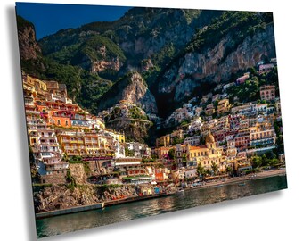 Puede incluir: Una impresión vibrante de un pueblo costero italiano enclavado en una ladera. Los edificios están pintados en una variedad de colores, incluyendo rojo, amarillo y naranja. El agua es de un azul profundo y el cielo está despejado.