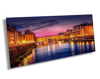 May include: A panoramic wall art print depicting the Ponte Vecchio bridge in Florence, Italy, at twilight. The scene features illuminated buildings along the Arno River, reflecting golden lights against a deep blue and vibrant purple sunset sky.