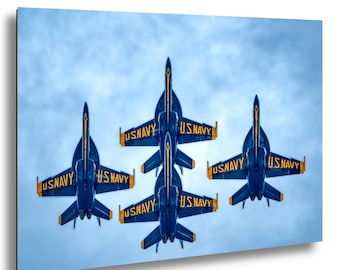 May include: Four blue U.S. Navy fighter jets flying in a tight formation against a cloudy sky. Each aircraft features yellow lettering that reads U.S. NAVY on the wings. The jets are positioned in a diamond-like arrangement, pointing upward.