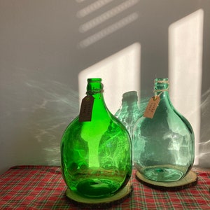 May include: Two green glass bottles with cork stoppers and brown paper tags that say "fresh" and "love" on them. The bottles are sitting on wooden rounds on a red and green plaid tablecloth.