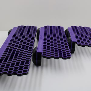 May include: Three purple honeycomb-shaped cooling pads of different sizes. The pads are made of a rigid plastic material and have a honeycomb pattern on the top surface. The pads are designed to elevate and cool laptops or other devices.