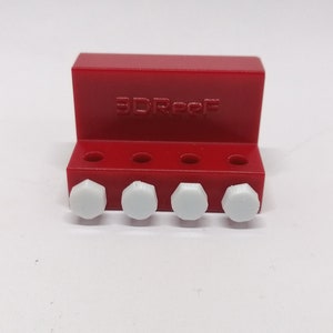 Puede incluir: Portaobjetos de plástico rojo con el texto "3D-REPF" impreso en la parte delantera. Cinco tuercas hexagonales de plástico blanco están unidas al soporte.