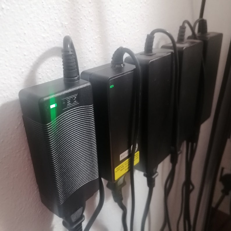 May include: Four black power adapters plugged into a wall socket. The adapters have green indicator lights.