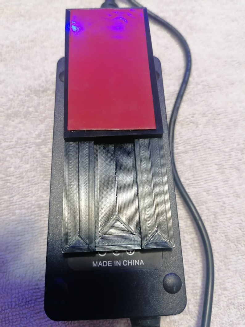 May include: A black power adapter with a red adhesive pad on top. The adapter has a black cord and the text "MADE IN CHINA" printed on the bottom.