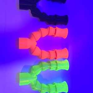 May include: Three flexible, articulated tubes in black, orange, and green. Each tube has a cylindrical base and a ribbed, bendable body. The background is a gradient of blue and purple.