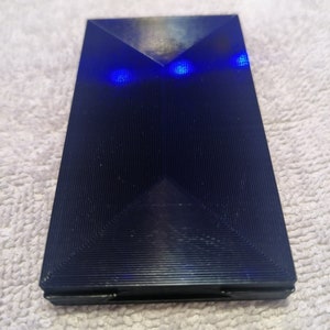 May include: A black, rectangular, textured object with two blue lights on the top.