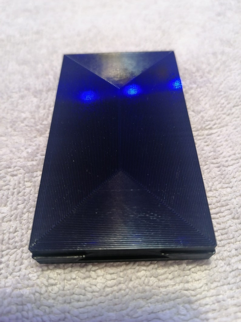 May include: A black, rectangular, textured object with two blue lights on the top.