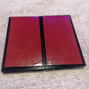 May include: Two black picture frames with red backing. The frames are closed and sitting on a white fluffy surface.