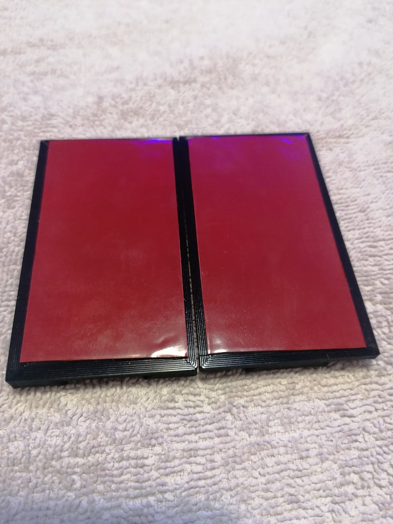 May include: Two black picture frames with red backing. The frames are closed and sitting on a white fluffy surface.