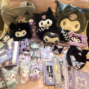 May include: A collection of Kuromi-themed merchandise, including plush toys, bags, a water bottle, hairbrush, notebooks, and stationery. The items feature a black and white color scheme with purple accents. The plush toys have a skull design. The items are arranged on a pink surface.
