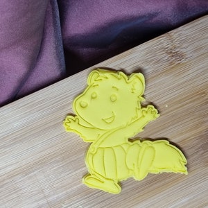 Puede incluir: Cortador de galletas de pl&aacute;stico amarillo en forma de ardilla de dibujos animados con una expresi&oacute;n feliz, vistiendo un mono y un sombrero.