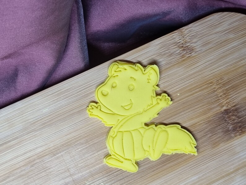 Puede incluir: Cortador de galletas de pl&aacute;stico amarillo en forma de ardilla de dibujos animados con una expresi&oacute;n feliz, vistiendo un mono y un sombrero.