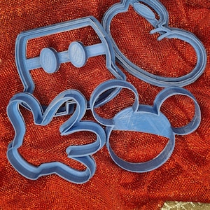 Peut inclure: Un ensemble de quatre emporte-pièces en plastique bleu. Les emporte-pièces sont en forme de tête de Mickey Mouse, d'une main, d'un cœur et de lunettes de soleil.