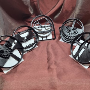 K&ouml;nnte beinhalten: F&uuml;nf schwarze Plastik-Ausstecher in Form von Figuren aus dem Film Nightmare Before Christmas. Die Ausstecher werden auf wei&szlig;en St&auml;ndern pr&auml;sentiert.