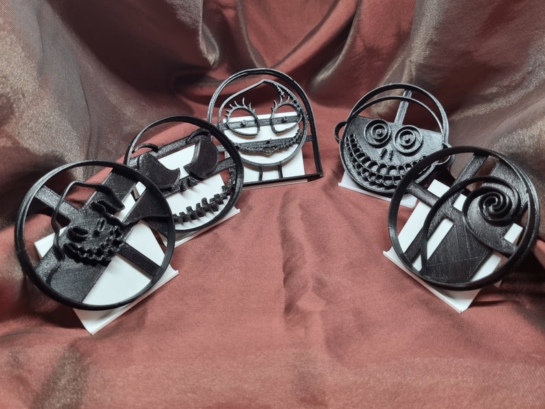 K&ouml;nnte beinhalten: F&uuml;nf schwarze Plastik-Ausstecher in Form von Figuren aus dem Film Nightmare Before Christmas. Die Ausstecher werden auf wei&szlig;en St&auml;ndern pr&auml;sentiert.