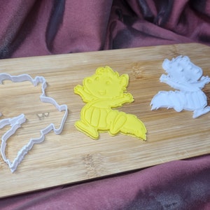 Puede incluir: Tres cortadores de galletas sobre una superficie de madera. Los cortadores tienen forma de animales de dibujos animados. Un cortador es amarillo y los otros dos son blancos.