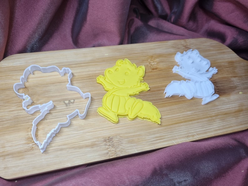 Puede incluir: Tres cortadores de galletas sobre una superficie de madera. Los cortadores tienen forma de animales de dibujos animados. Un cortador es amarillo y los otros dos son blancos.